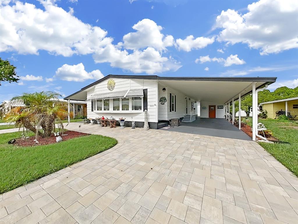A white manufactured home features a paved driveway, a large carport, and a landscaped front yard — 5022 FOXWOOD BLVD, LAKELAND, FL