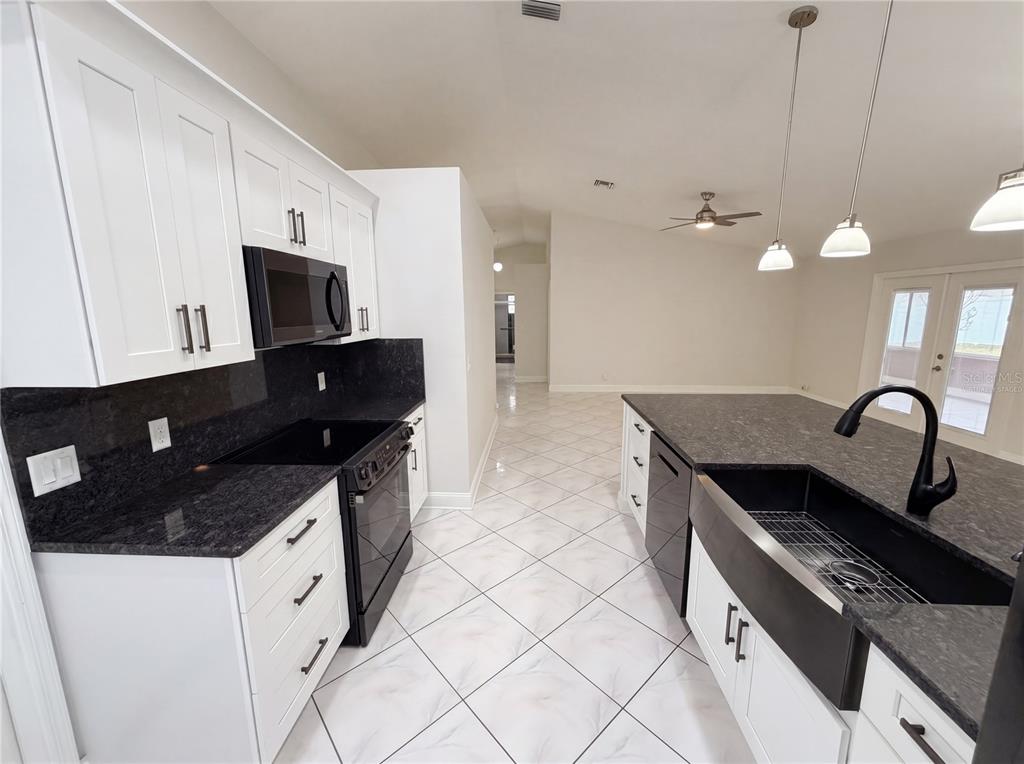 A kitchen features white cabinets, dark granite countertops, a farmhouse sink, and tiled floors — 4614 ZOLTAN DRIVE, TITUSVILLE, FL