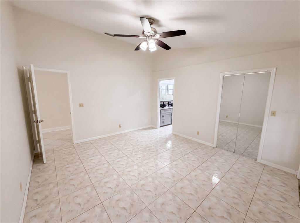 A bedroom with light-colored tile flooring, a ceiling fan, and mirrored closet doors — 4614 ZOLTAN DRIVE, TITUSVILLE, FL
