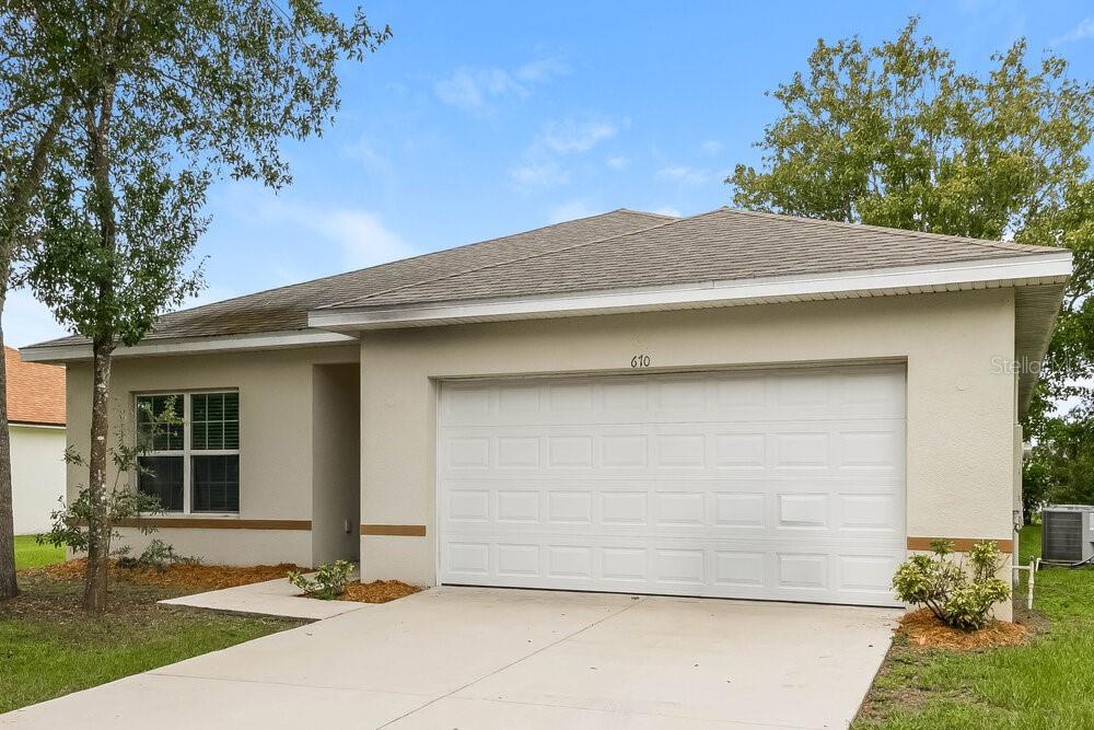 A single-story house with a beige stucco exterior, a two-car garage, and a concrete driveway — 670 BASINGSTOKE COURT, KISSIMMEE, FL