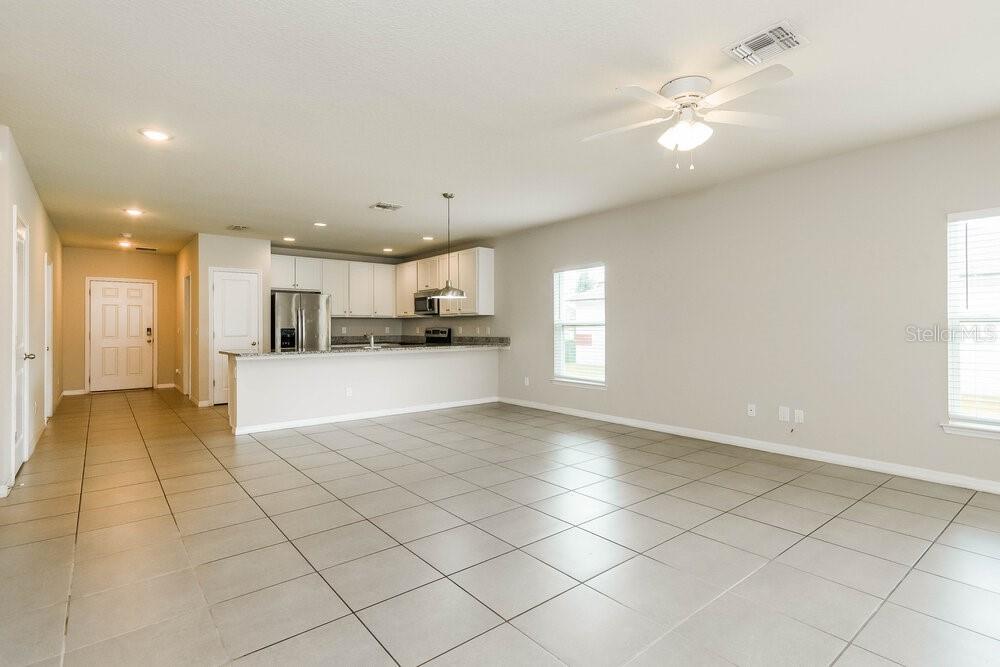 An open-concept kitchen and living area features light tile flooring and white cabinetry — 670 BASINGSTOKE COURT, KISSIMMEE, FL