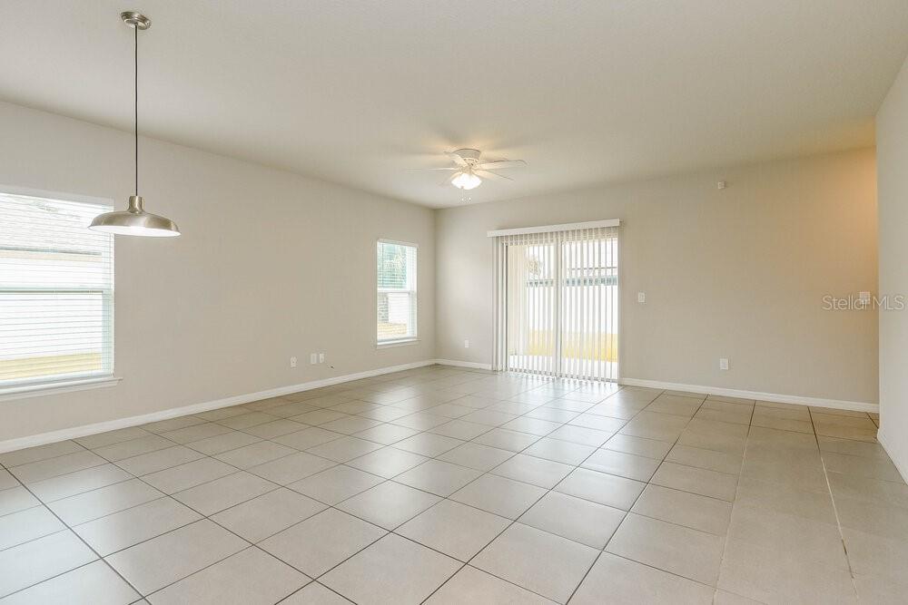 An open-concept living area features light-colored tile flooring, neutral walls, and a sliding glass door — 670 BASINGSTOKE COURT, KISSIMMEE, FL