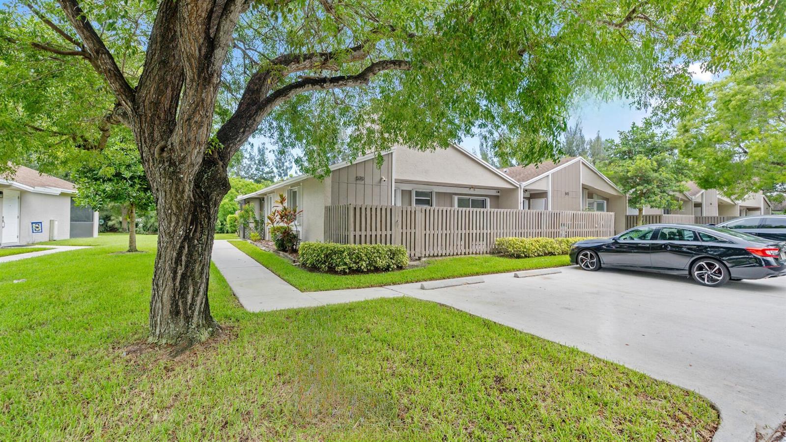 A single-story residential building with a wooden privacy fence, a concrete driveway, and large trees — 570 Woodgate Circle # A, Sunrise FL 33326, SUNRISE, FL