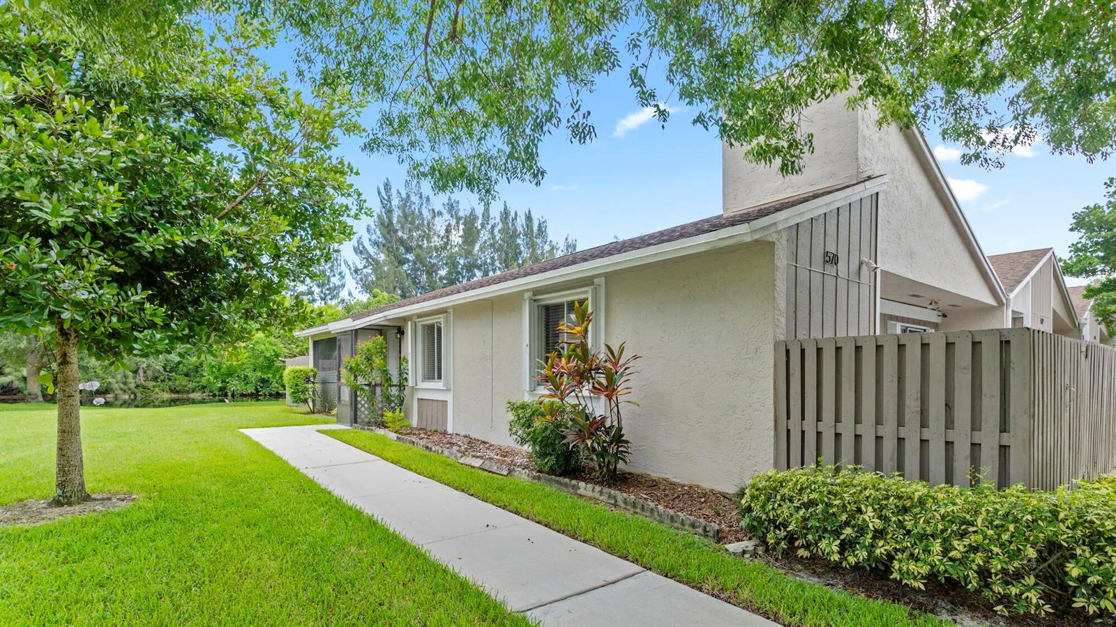 A single-story house with a beige stucco exterior, a wooden fence, and a concrete walkway — 570 Woodgate Circle # A, Sunrise FL 33326, SUNRISE, FL