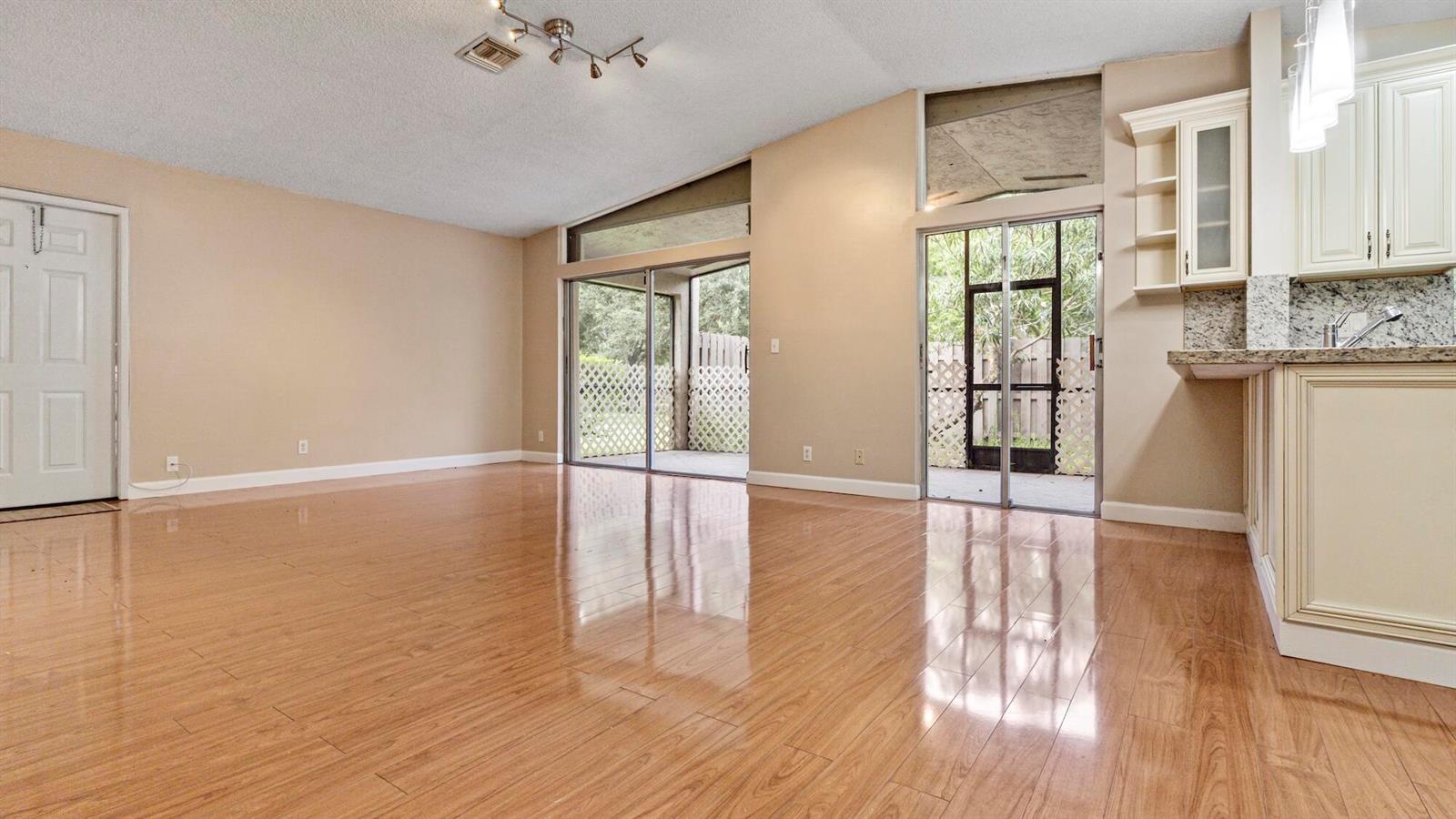 A living room with wood-look flooring, beige walls, and sliding glass doors leading to a patio — 570 Woodgate Circle # A, Sunrise FL 33326, SUNRISE, FL