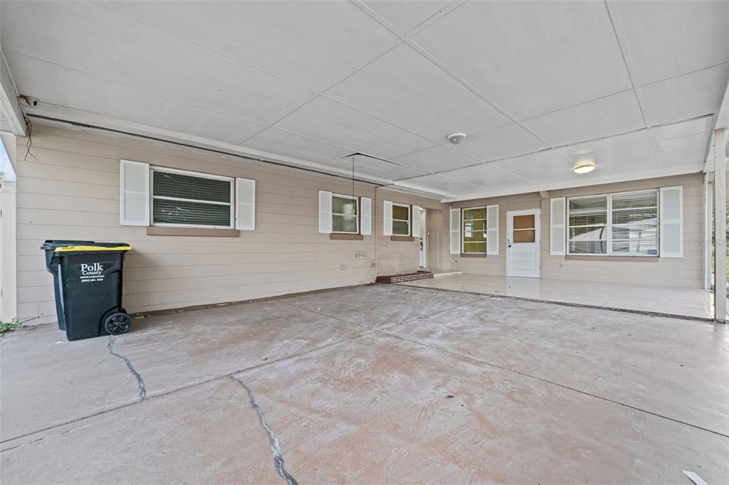 A covered concrete carport area features beige siding, multiple windows with shutters, and a white door — 912 AVENUE T SE, WINTER HAVEN, FL