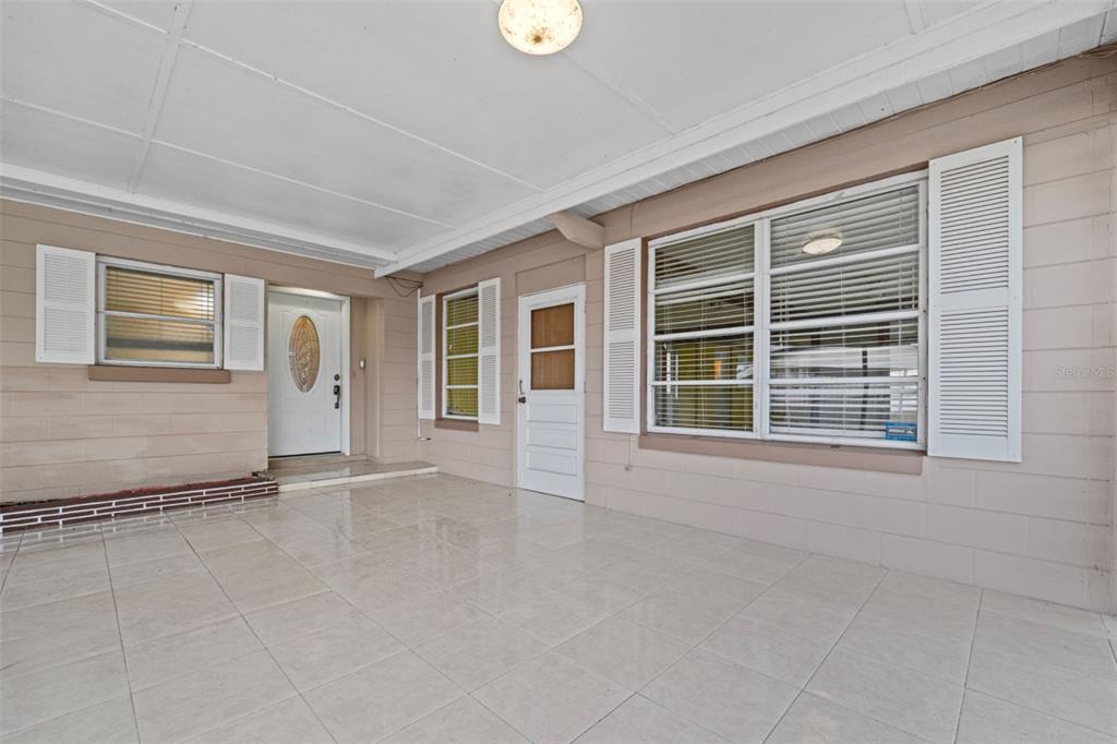 A covered patio features light-colored tile flooring, beige exterior walls, and multiple windows with shutters — 912 AVENUE T SE, WINTER HAVEN, FL