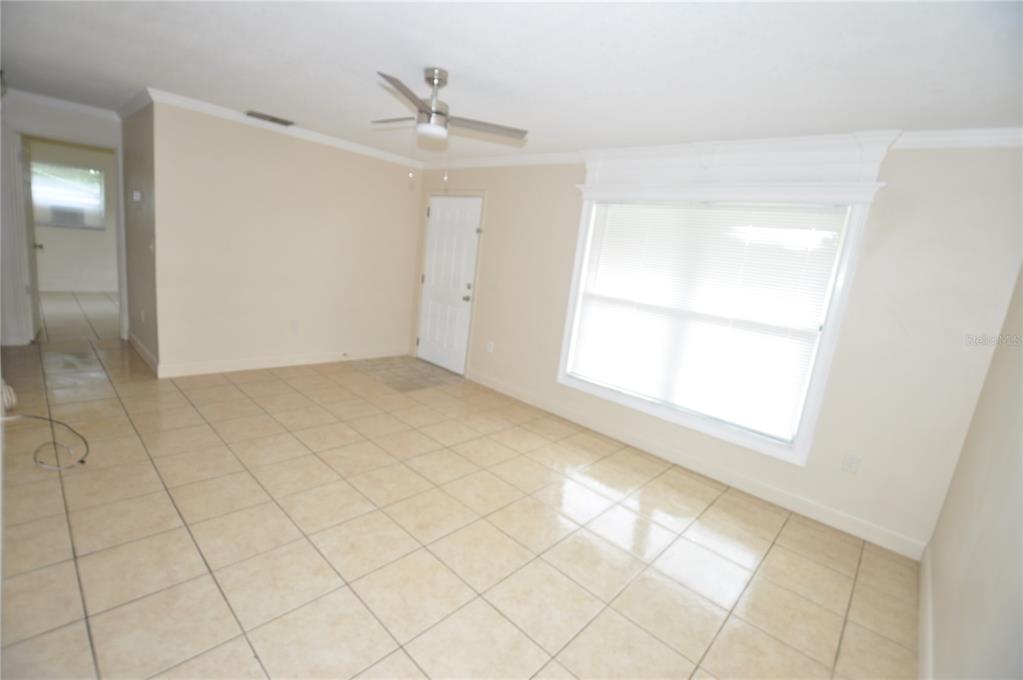 An empty living room features beige tile flooring, a ceiling fan, and a large window — 1624 MERRICK ROAD, LAKELAND, FL