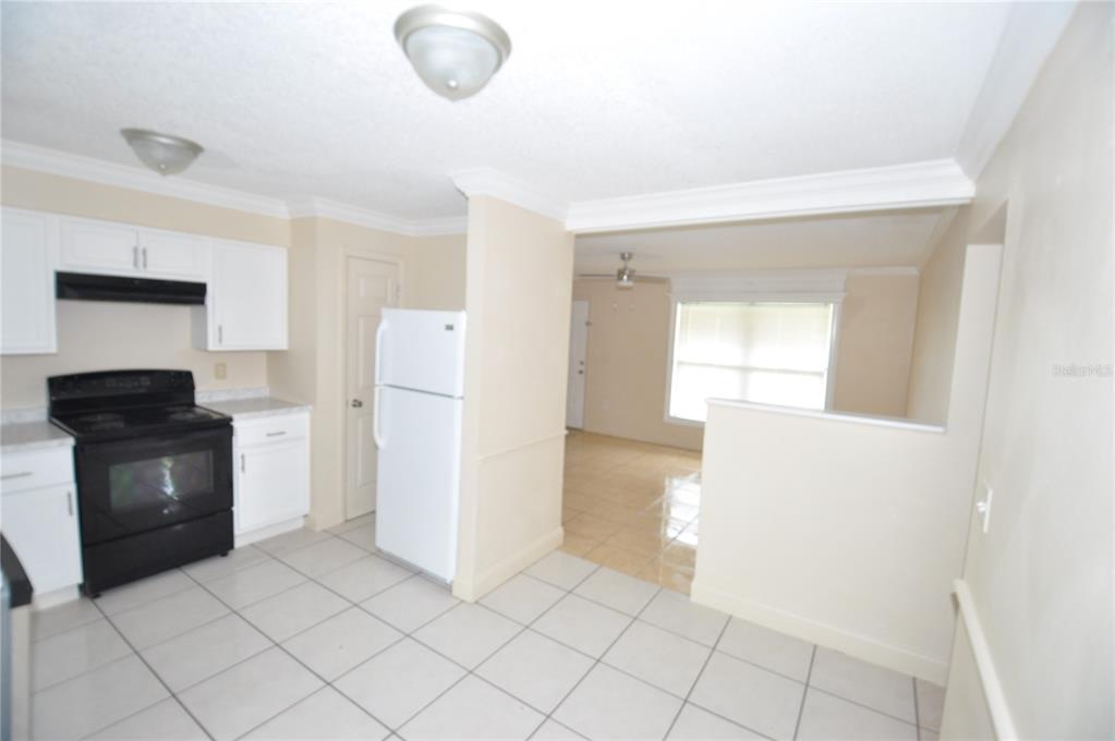 A kitchen with white cabinets, black appliances, and tile flooring opens to a living area — 1624 MERRICK ROAD, LAKELAND, FL