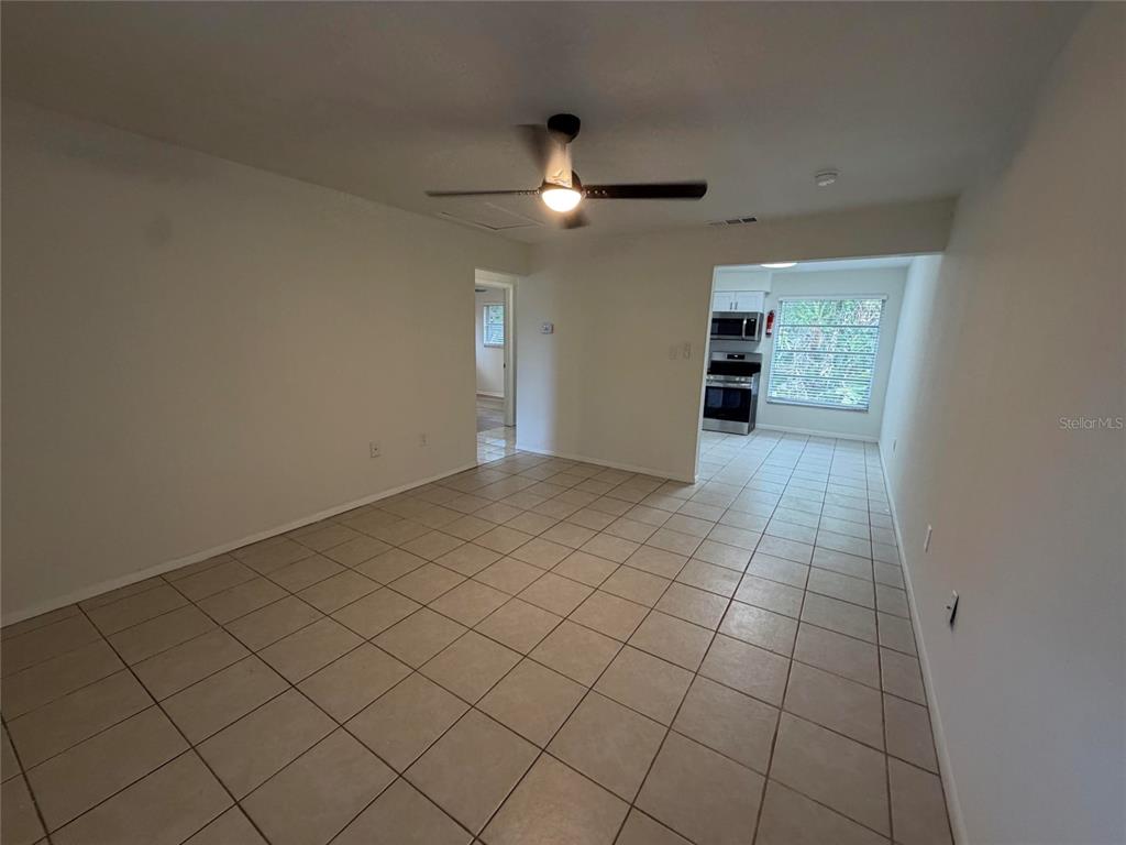 An interior view shows a tiled living area leading to a kitchen with a window — 460 BELTREES STREET, DUNEDIN, FL