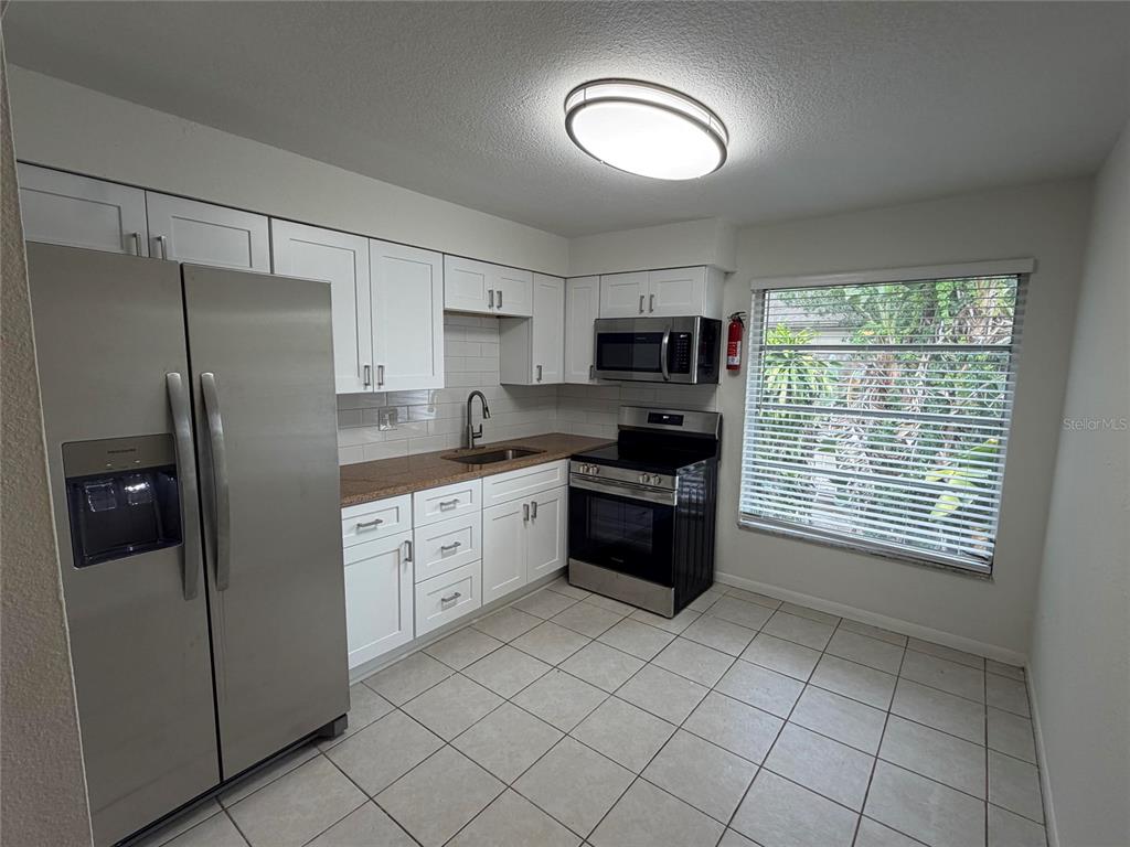 A kitchen features white cabinets, stainless steel appliances, brown countertops, and light-colored tile flooring — 460 BELTREES STREET, DUNEDIN, FL