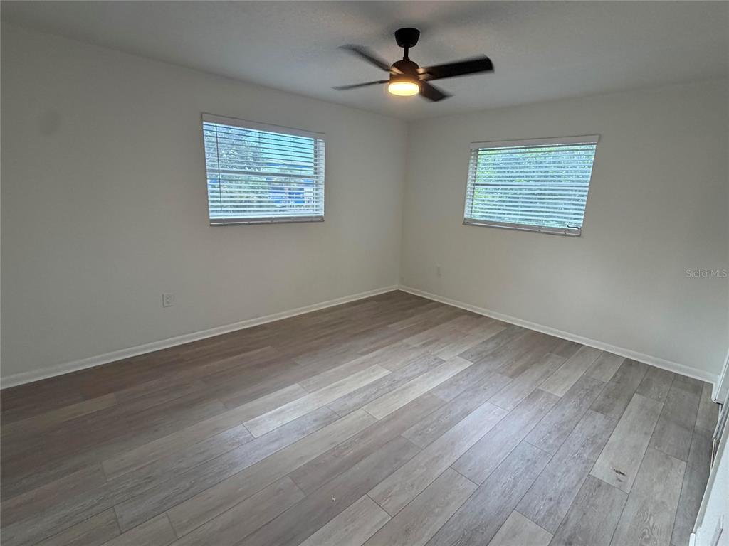 An empty bedroom features light-colored wood-look flooring, white walls, two windows, and a ceiling fan — 460 BELTREES STREET, DUNEDIN, FL