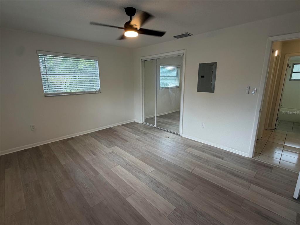 A bedroom with wood-look flooring, a ceiling fan, mirrored closet doors, and an electrical panel — 460 BELTREES STREET, DUNEDIN, FL