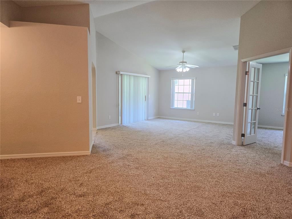 A carpeted living room features a vaulted ceiling, a ceiling fan, and sliding glass doors — 17974 SE 115TH CIRCLE, SUMMERFIELD, FL
