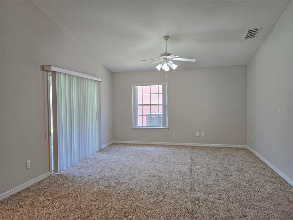 An empty room features beige carpet, a ceiling fan, a window, and sliding glass doors — 17974 SE 115TH CIRCLE, SUMMERFIELD, FL