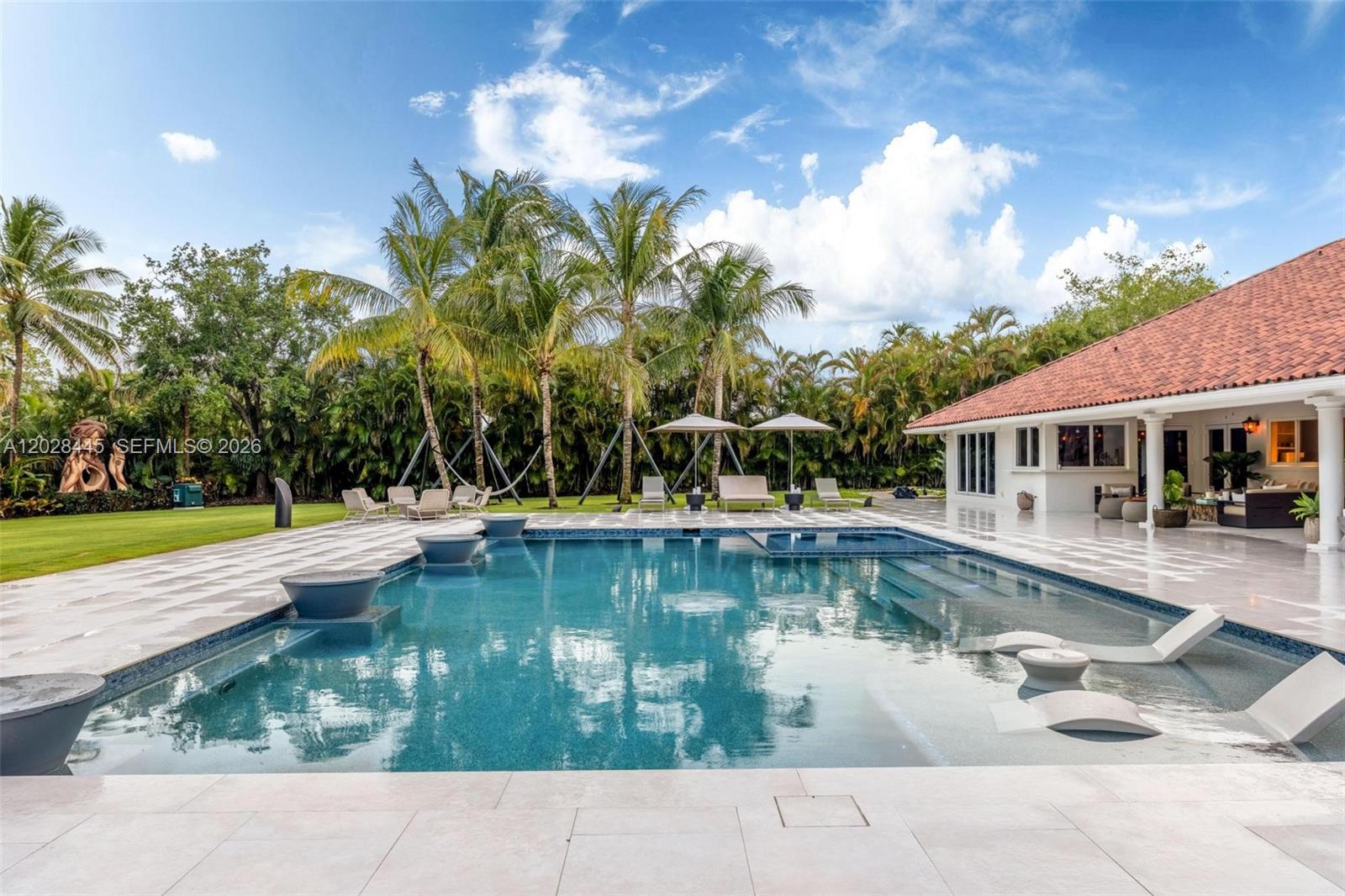A swimming pool with lounge chairs and fire bowls sits on a patio by a house — 8251 Old Cutler Rd, Coral Gables FL 33143, CORAL GABLES, FL