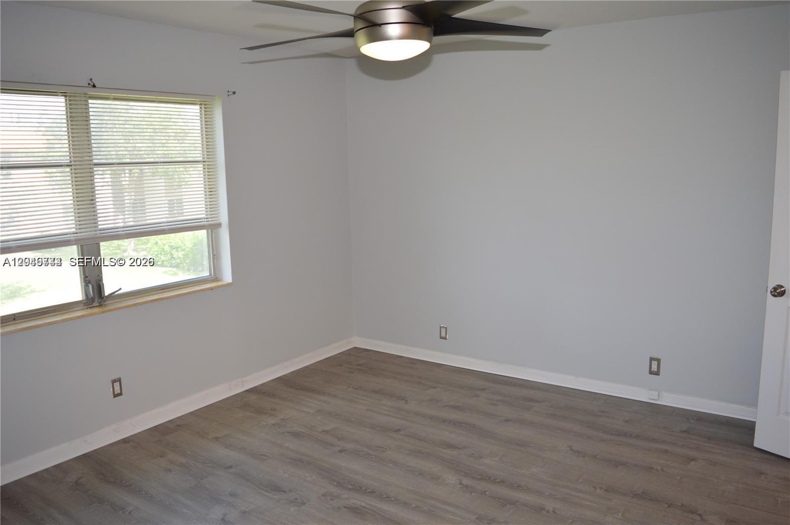 An empty bedroom features light gray walls, wood-look flooring, a ceiling fan, and a window — 9 NE 19th Ct # 204C, Wilton Manors FL 33305, WILTON MANORS, FL