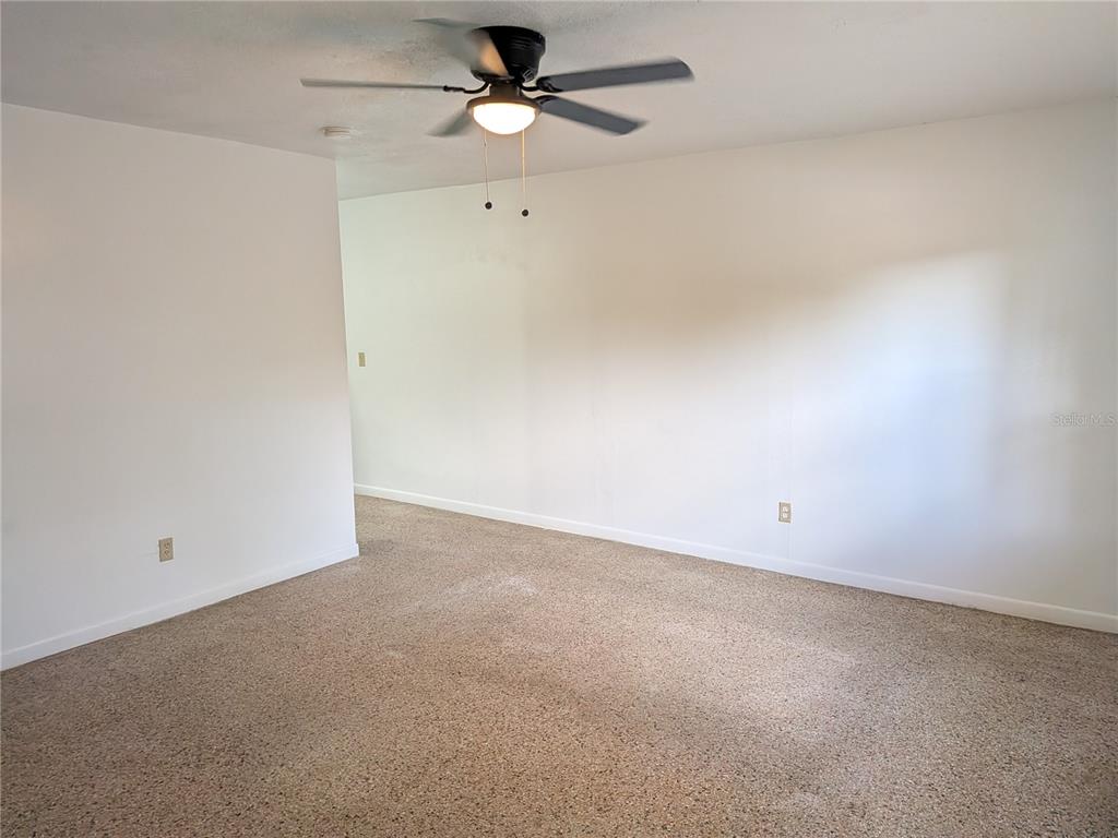 An empty room features beige carpet, white walls, and a ceiling fan with a light — 2461 44, OCALA, FL