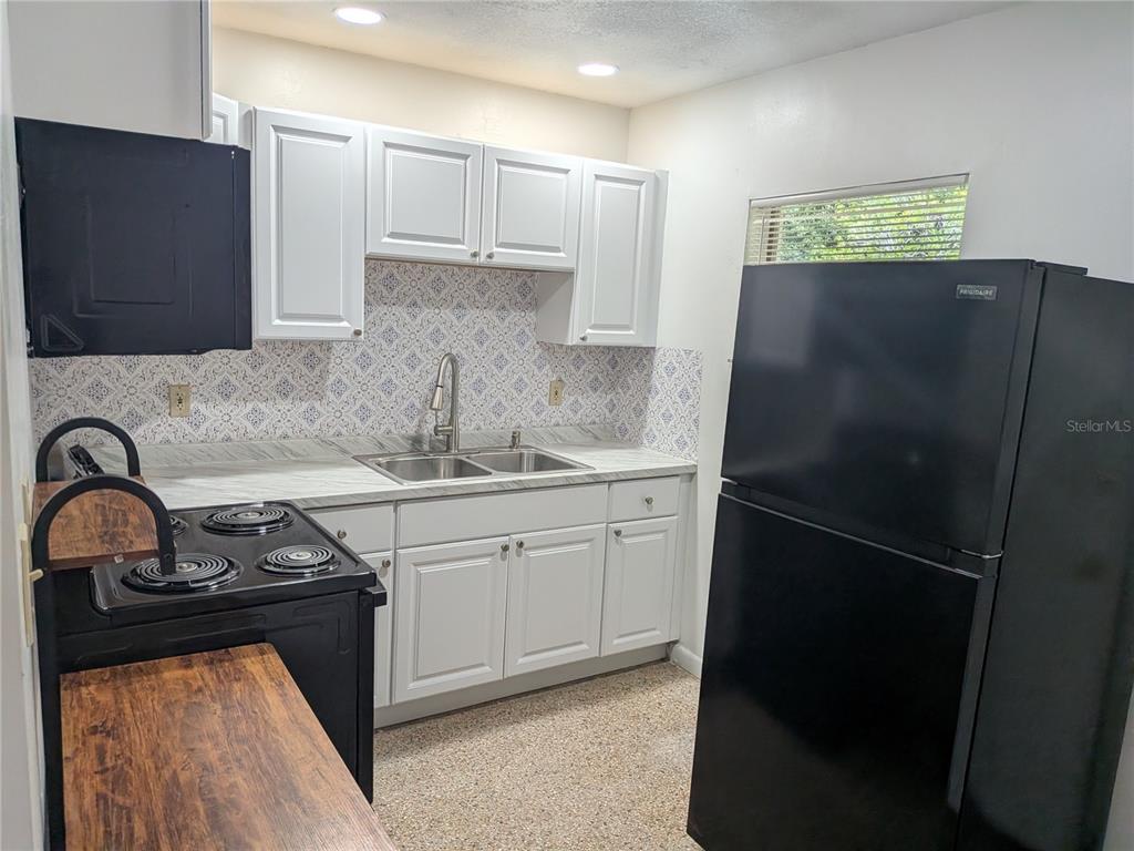 A kitchen features white cabinets, a patterned backsplash, black appliances, and a wood-look counter — 2461 44, OCALA, FL
