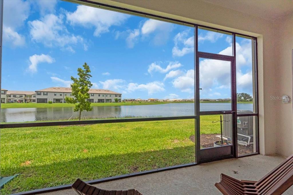 A screened-in patio overlooks a grassy lawn and a lake with distant residential buildings — 15131 SUNNY DAY DRIVE, BRADENTON, FL