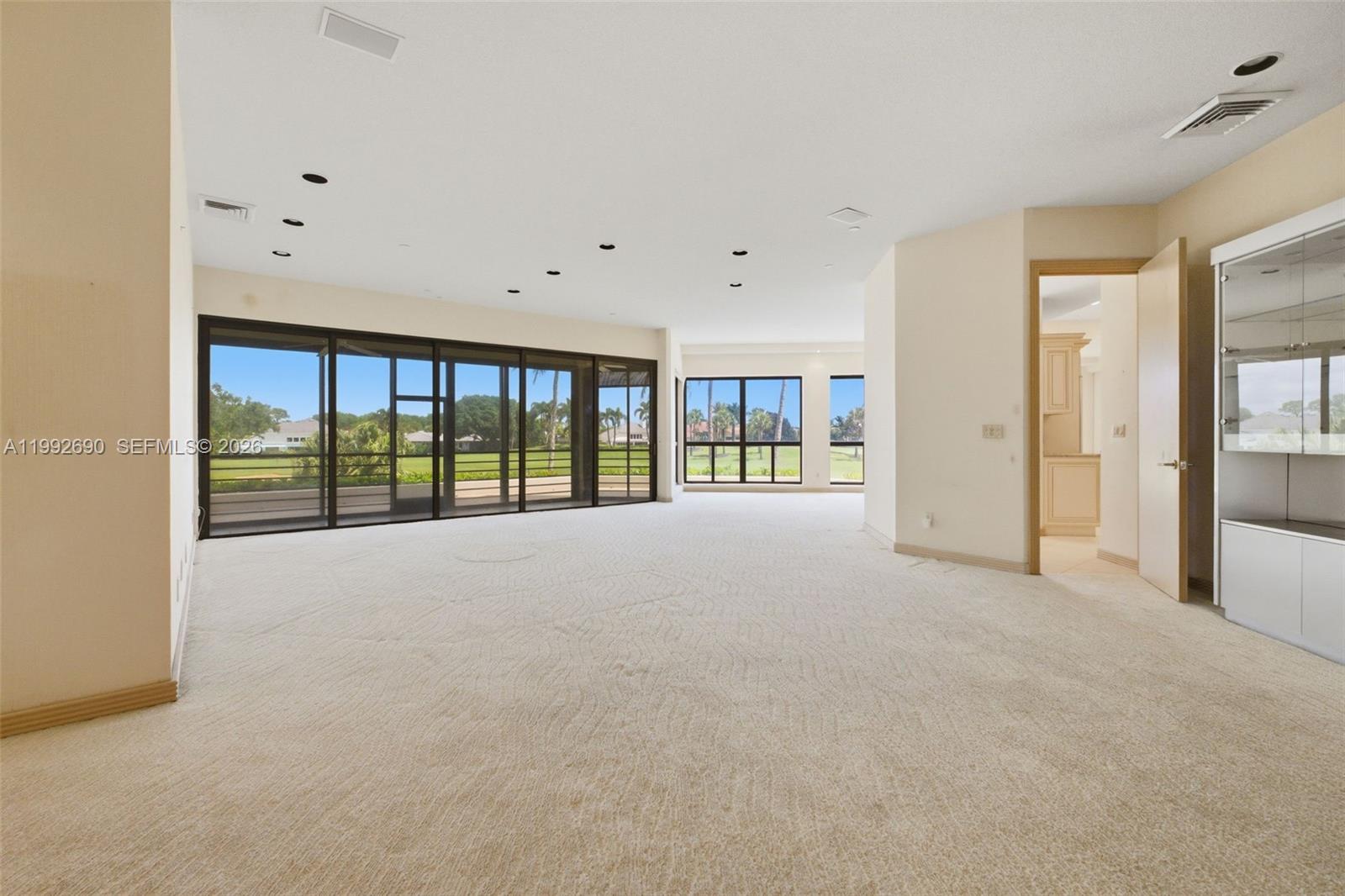 A spacious, carpeted living room features large glass sliding doors overlooking a golf course — 7383 Orangewood Ln # 301, Boca Raton FL 33433, BOCA RATON, FL