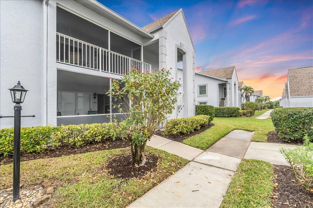 An exterior view of a two-story apartment building with screened balconies and a paved walkway — 6713 STONE RIVER ROAD UNIT 206, BRADENTON, FL