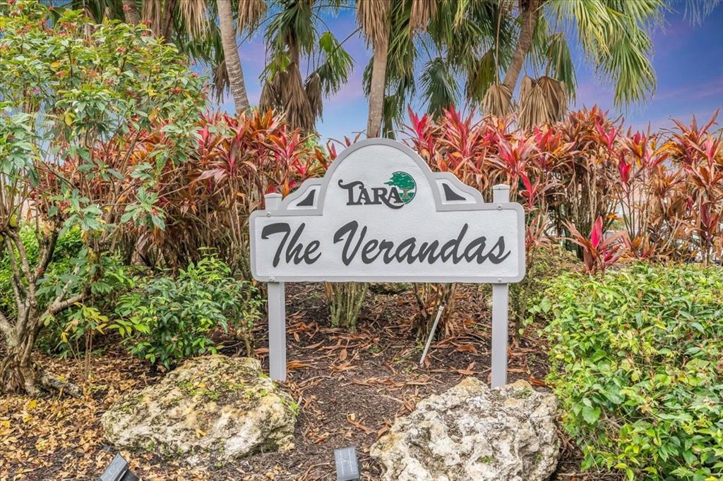 A sign for The Verandas at Tara stands in a garden with palm trees — 6713 STONE RIVER ROAD UNIT 206, BRADENTON, FL