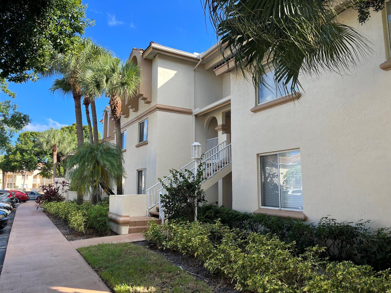 A multi-story apartment building exterior features beige stucco walls, white stairs, and palm trees — 18106 Glenmoor Drive, West Palm Beach FL 33409, WEST PALM BEACH, FL