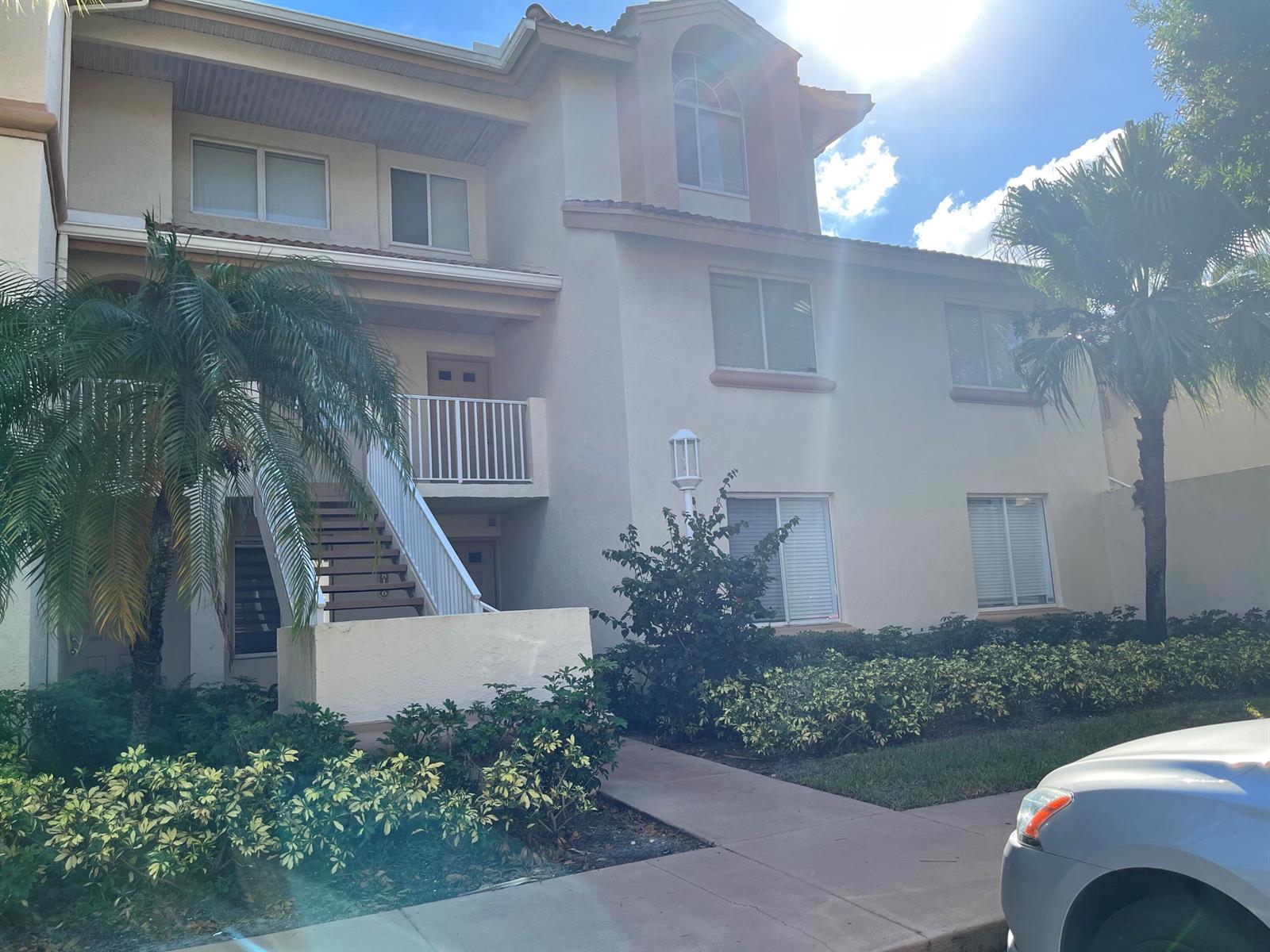A two-story apartment building with beige stucco walls, a staircase, and surrounding landscaping — 18106 Glenmoor Drive, West Palm Beach FL 33409, WEST PALM BEACH, FL