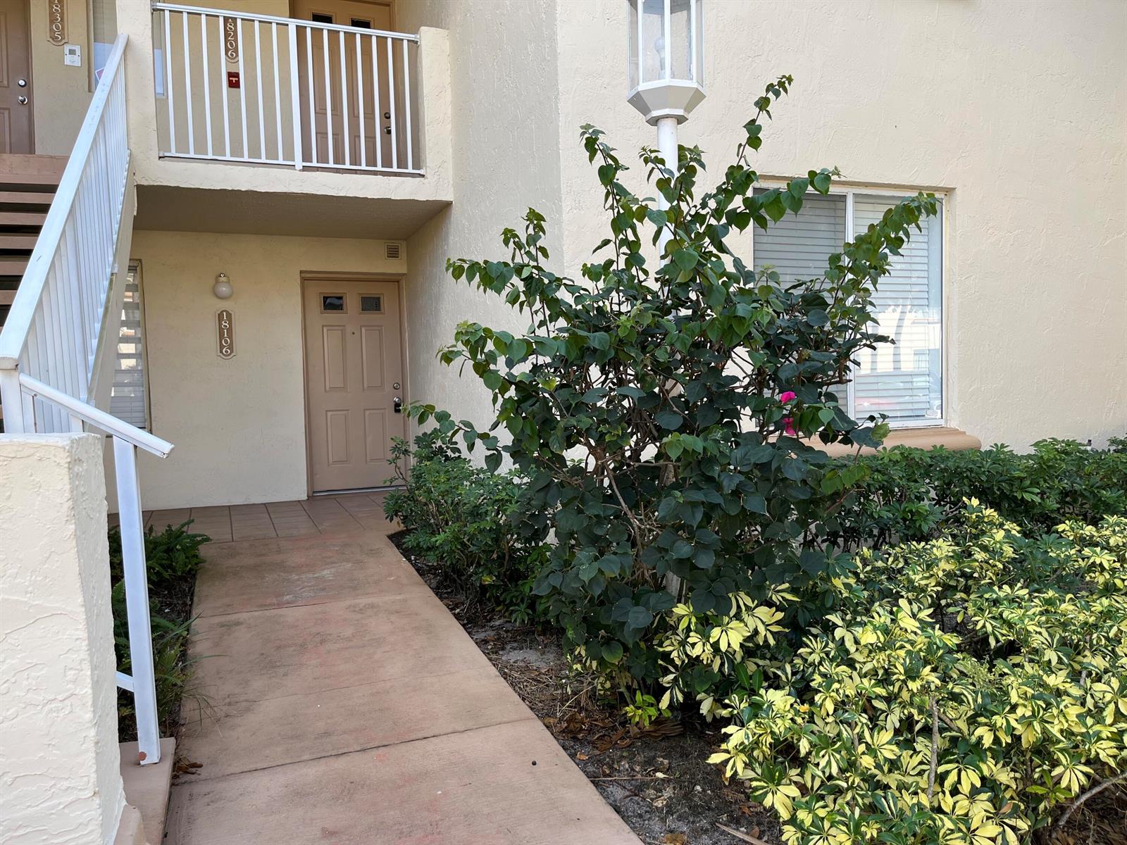 A concrete walkway leads to the tan front door of a two-story apartment building — 18106 Glenmoor Drive, West Palm Beach FL 33409, WEST PALM BEACH, FL