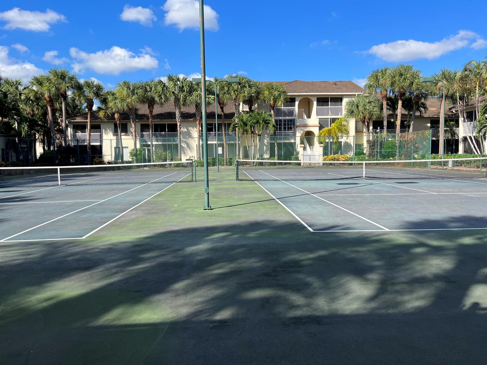 A view of two outdoor tennis courts with a multi-story apartment building in the background — 18106 Glenmoor Drive, West Palm Beach FL 33409, WEST PALM BEACH, FL