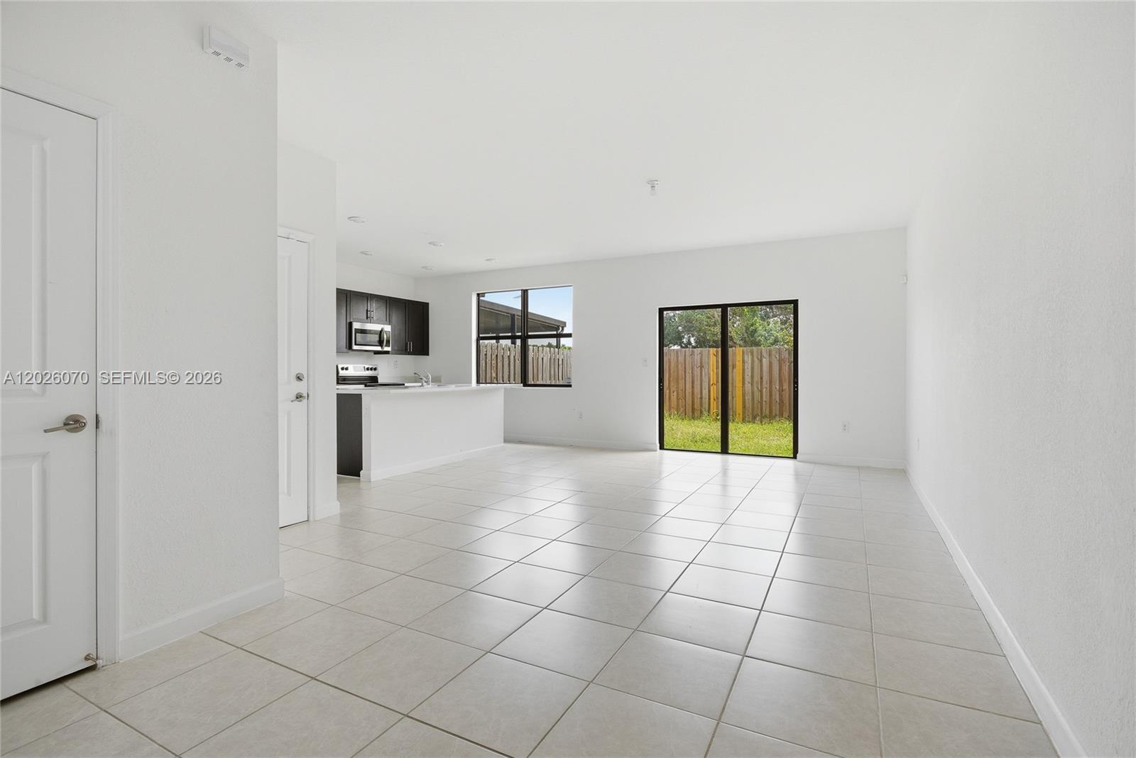 An open-concept living area features white tile floors, a kitchen with dark cabinets, and sliding doors — 10218 SW 231st Ln, Cutler Bay FL 33190, CUTLER BAY, FL