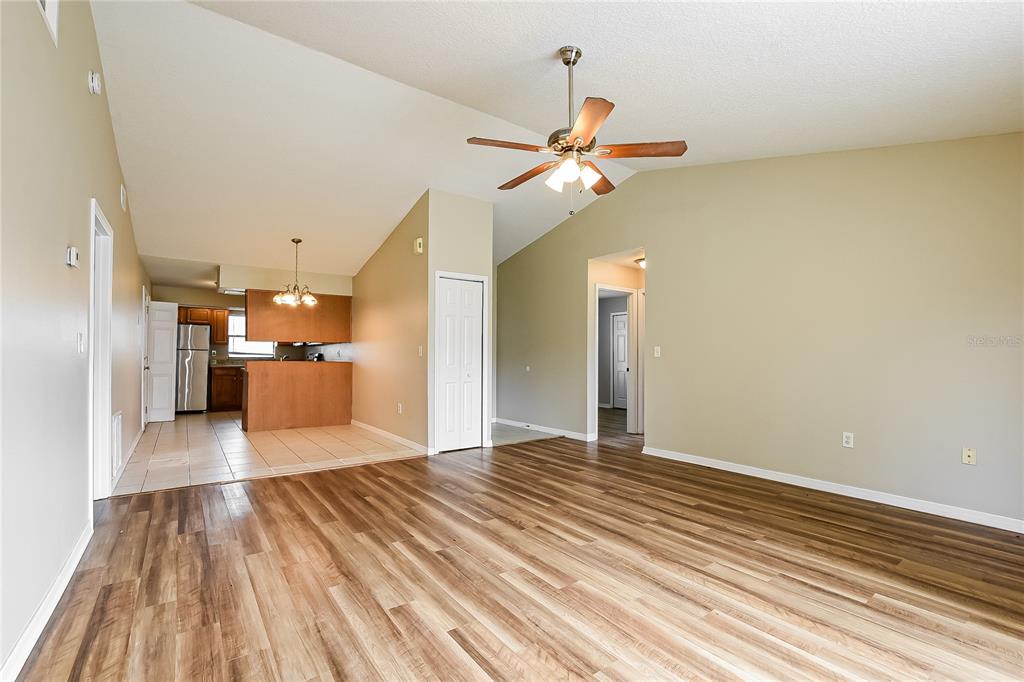 A living room with wood-look flooring and a vaulted ceiling opens to a tiled kitchen — 224 COBALT DRIVE, KISSIMMEE, FL