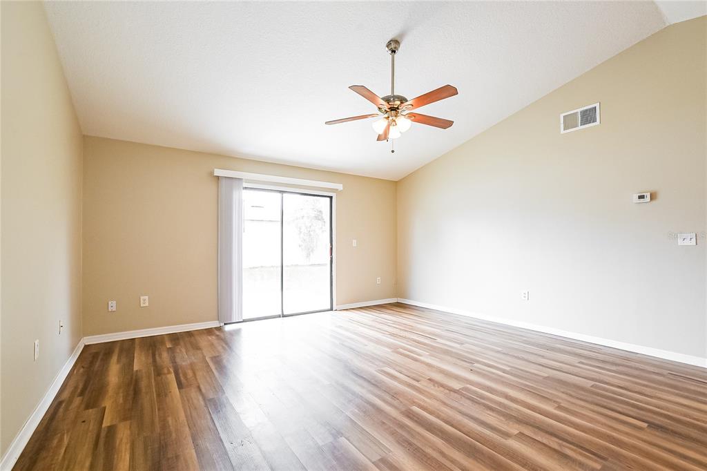 An empty living room features light tan walls, wood-look flooring, and a ceiling fan — 224 COBALT DRIVE, KISSIMMEE, FL