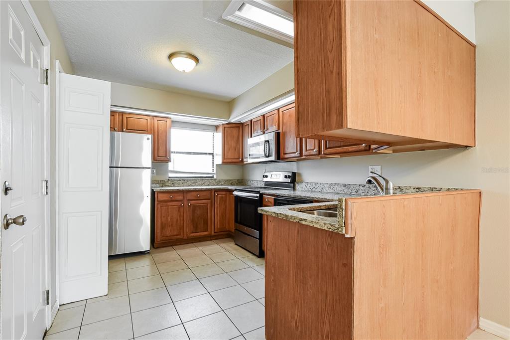 A kitchen features wood cabinets, granite countertops, stainless steel appliances, and light-colored tile flooring — 224 COBALT DRIVE, KISSIMMEE, FL