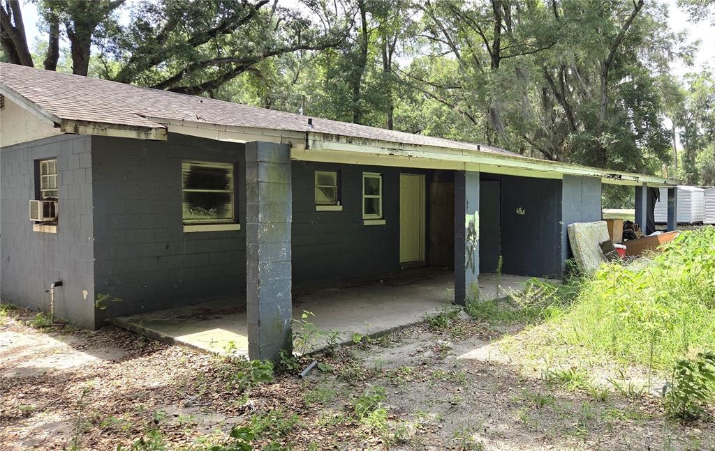 A single-story gray concrete block house features a covered porch and an overgrown yard — 521-535 NW 19TH AVENUE, OCALA, FL