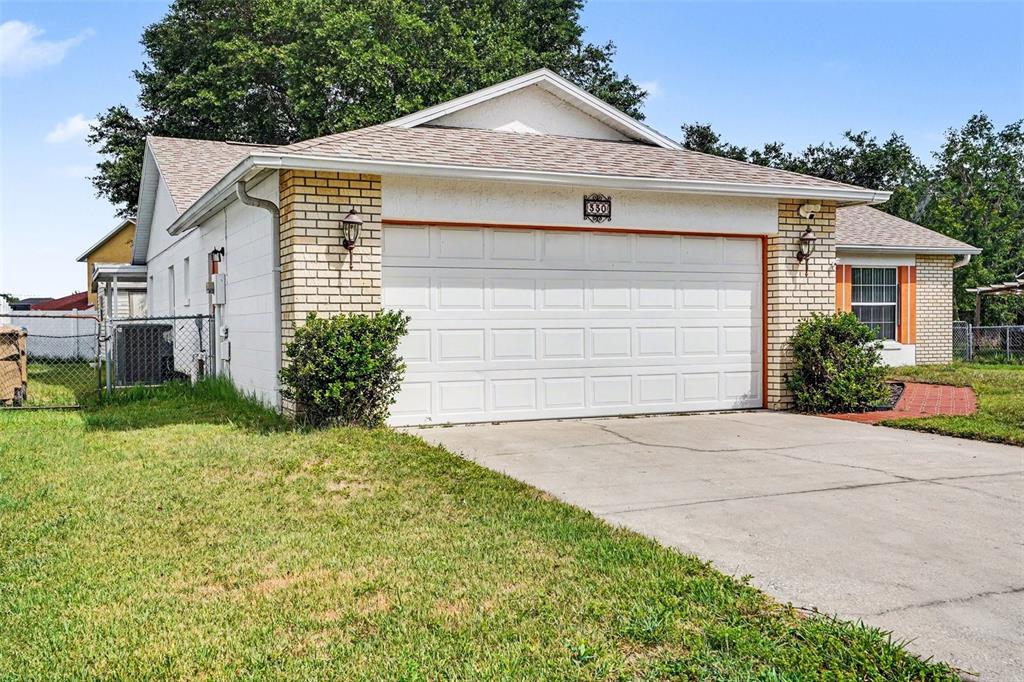 A single-story house with a white garage door, brick accents, and a concrete driveway — 330 CORTEZ COURT, KISSIMMEE, FL