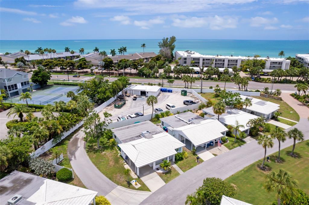 An aerial view shows a coastal residential complex with white-roofed buildings, palm trees, and tennis courts — 546 SPANISH DRIVE S, LONGBOAT KEY, FL