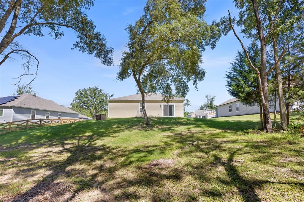 The backyard of a tan house features a grassy slope, mature trees, and wooden fencing — 15451 NW 121ST PLACE, ALACHUA, FL