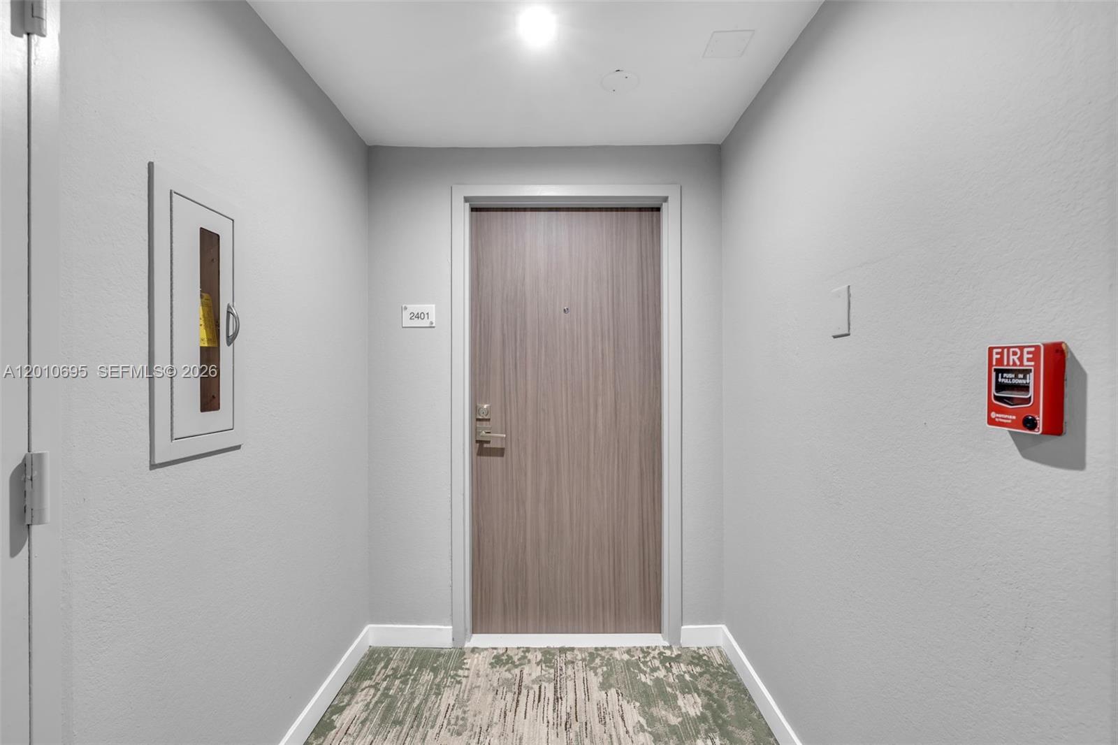 A hallway features a wooden door numbered 2401, a fire alarm, and a recessed cabinet — 2555 Collins Ave # 2401, Miami Beach FL 33140, MIAMI BEACH, FL