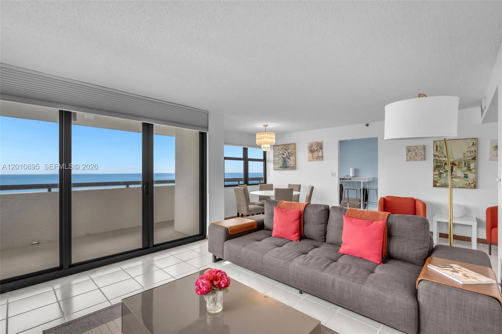 A living room with a gray sofa, tile floors, and a balcony overlooking the ocean — 2555 Collins Ave # 2401, Miami Beach FL 33140, MIAMI BEACH, FL