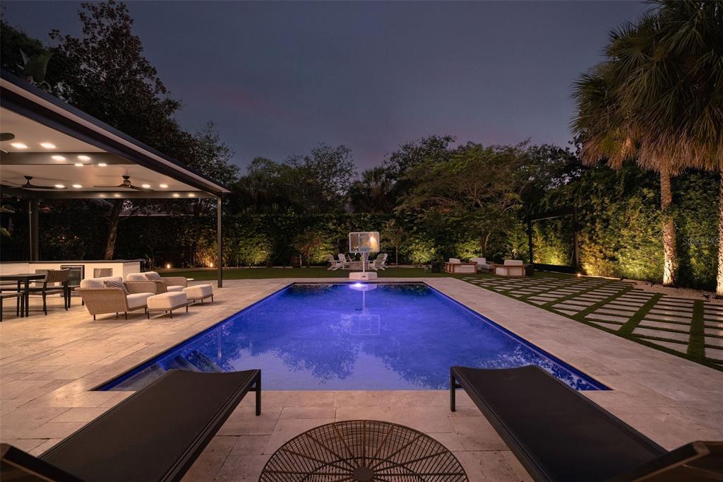 A backyard at night features a rectangular swimming pool, a covered patio, and lounge chairs — 906 ALHAMBRA COURT, ORLANDO, FL