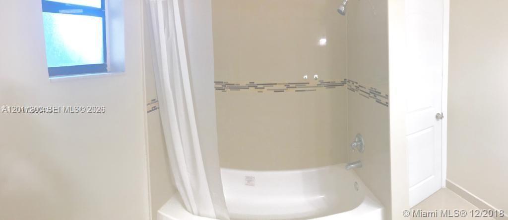 A bathroom features a white bathtub with a shower head and tan tiled walls — 11447 SW 33rd Ln # 0, Miami FL 33165, MIAMI, FL