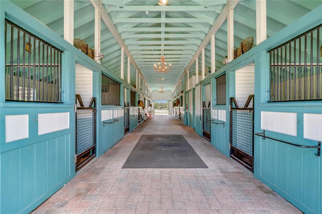 A bright, teal-painted horse stable aisle features brick flooring, chandeliers, and multiple stall doors — 3287 N COUNTY ROAD 426, GENEVA, FL