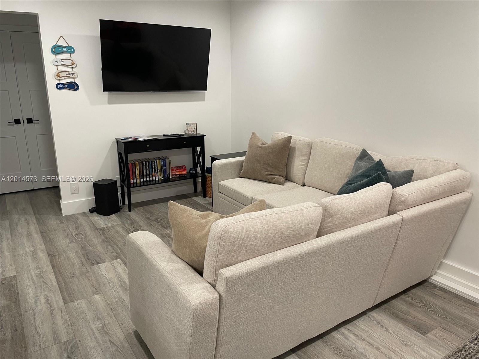 A living room features a wall-mounted television, a black console table, and a beige sofa — 326 Wilson St # 106, Hollywood FL 33019, HOLLYWOOD, FL