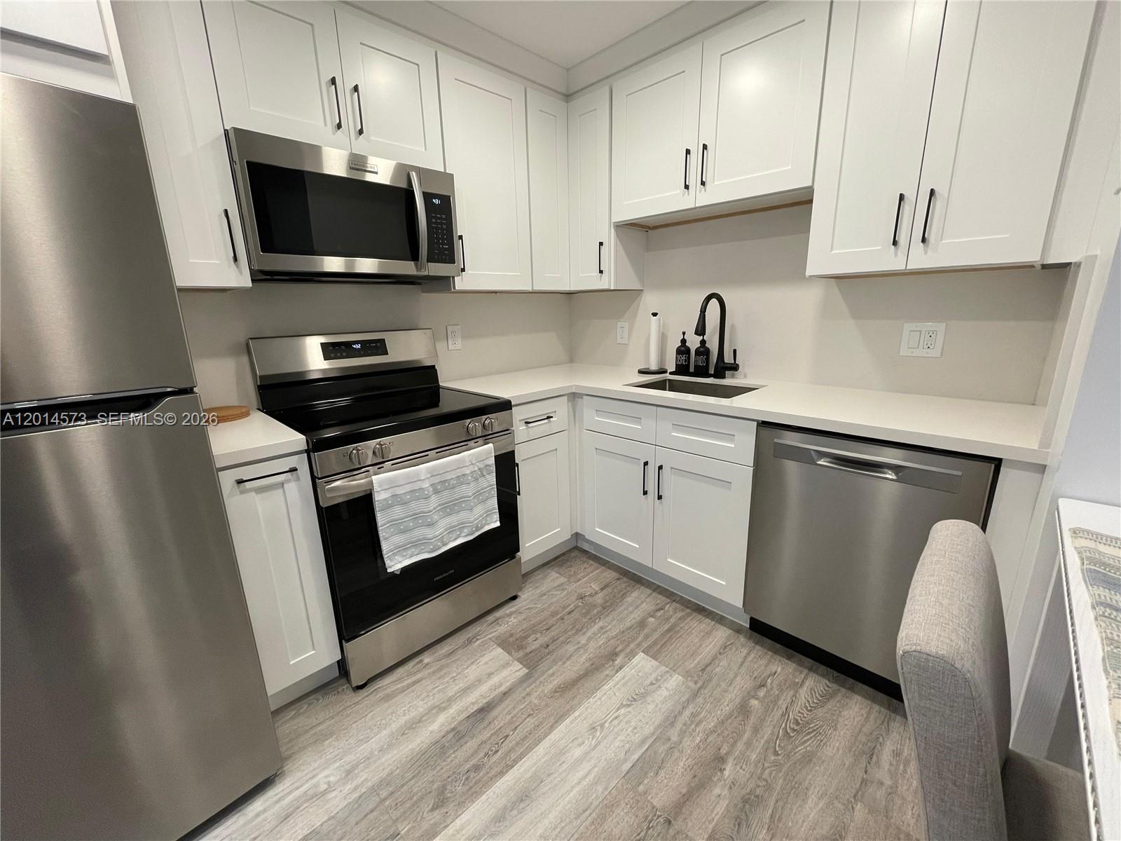 A kitchen features white cabinets, stainless steel appliances, a black faucet, and light wood flooring — 326 Wilson St # 106, Hollywood FL 33019, HOLLYWOOD, FL