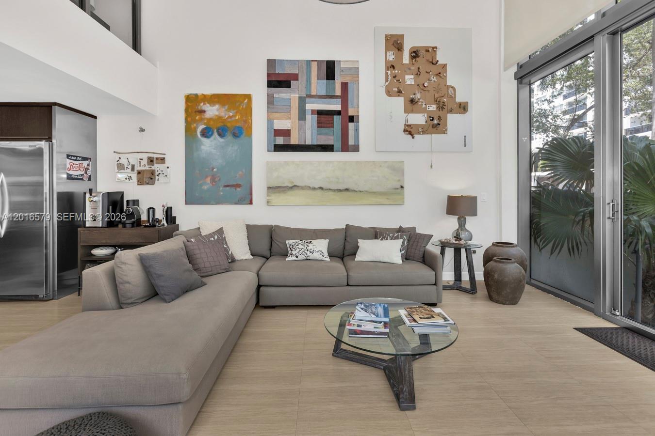 A living room features a grey sectional sofa, a glass coffee table, and wall art — 6000 Collins Ave # 129, Miami Beach FL 33140, MIAMI BEACH, FL