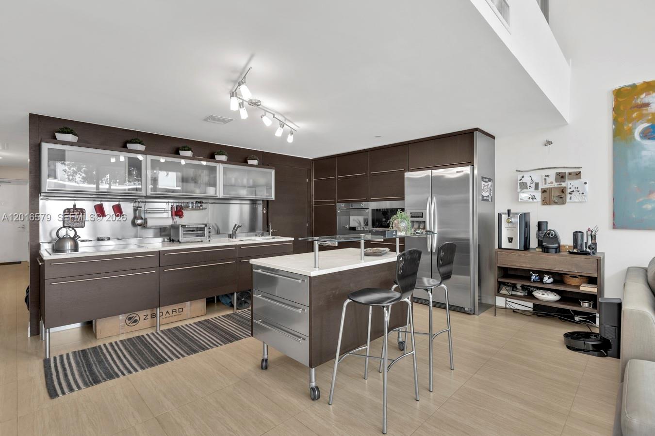 A modern kitchen features dark wood cabinetry, stainless steel appliances, and a mobile center island — 6000 Collins Ave # 129, Miami Beach FL 33140, MIAMI BEACH, FL
