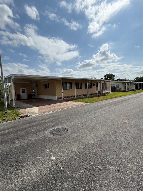 A tan mobile home with a carport sits along a paved street under a cloudy sky — 2055 S FLORAL AVENUE UNIT 175, BARTOW, FL