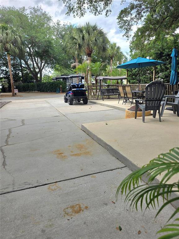 A concrete patio area features a golf cart, outdoor seating, and a blue umbrella — 218 HORSESHOE BEND, LAKE WALES, FL